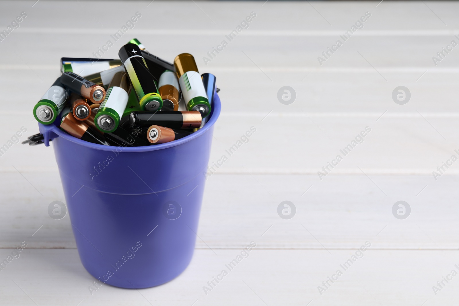 Image of Used batteries in bucket on white wooden table, space for text