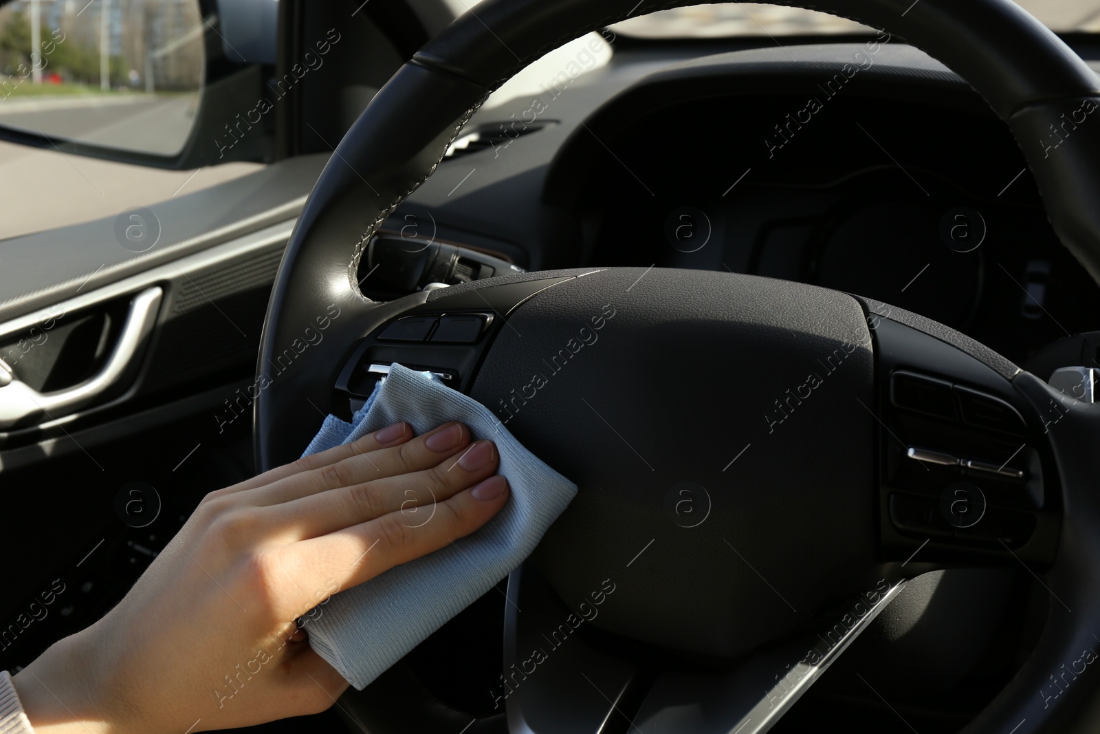 Photo of Woman cleaning steering wheel with rag in car, closeup