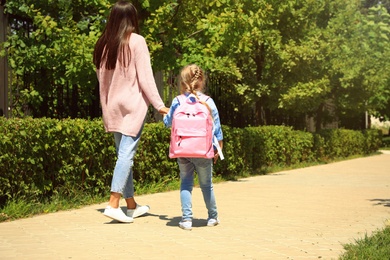 Photo of Young mother taking her little child to school through park