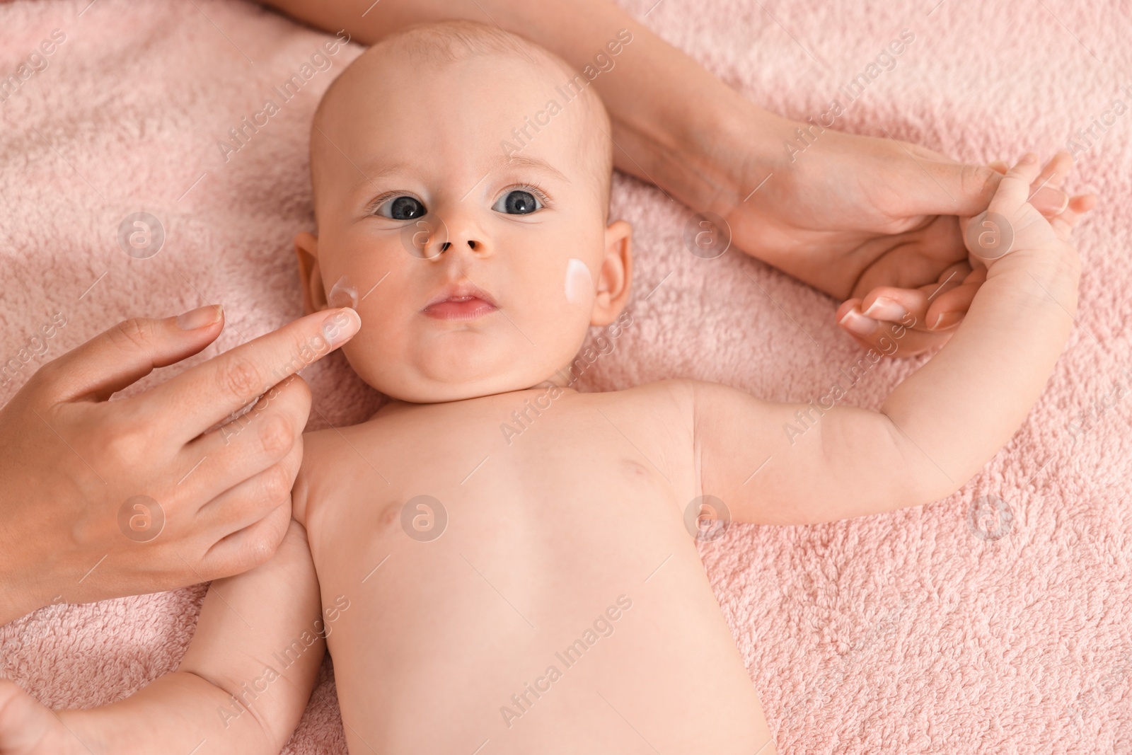 Photo of Woman applying cream onto baby`s face on bed, closeup