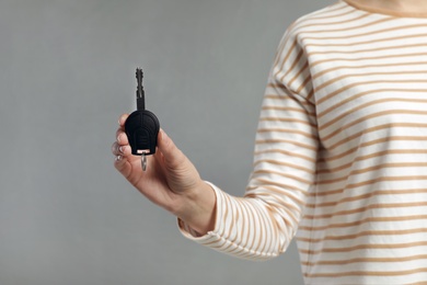 Young woman holding car key on grey background, closeup