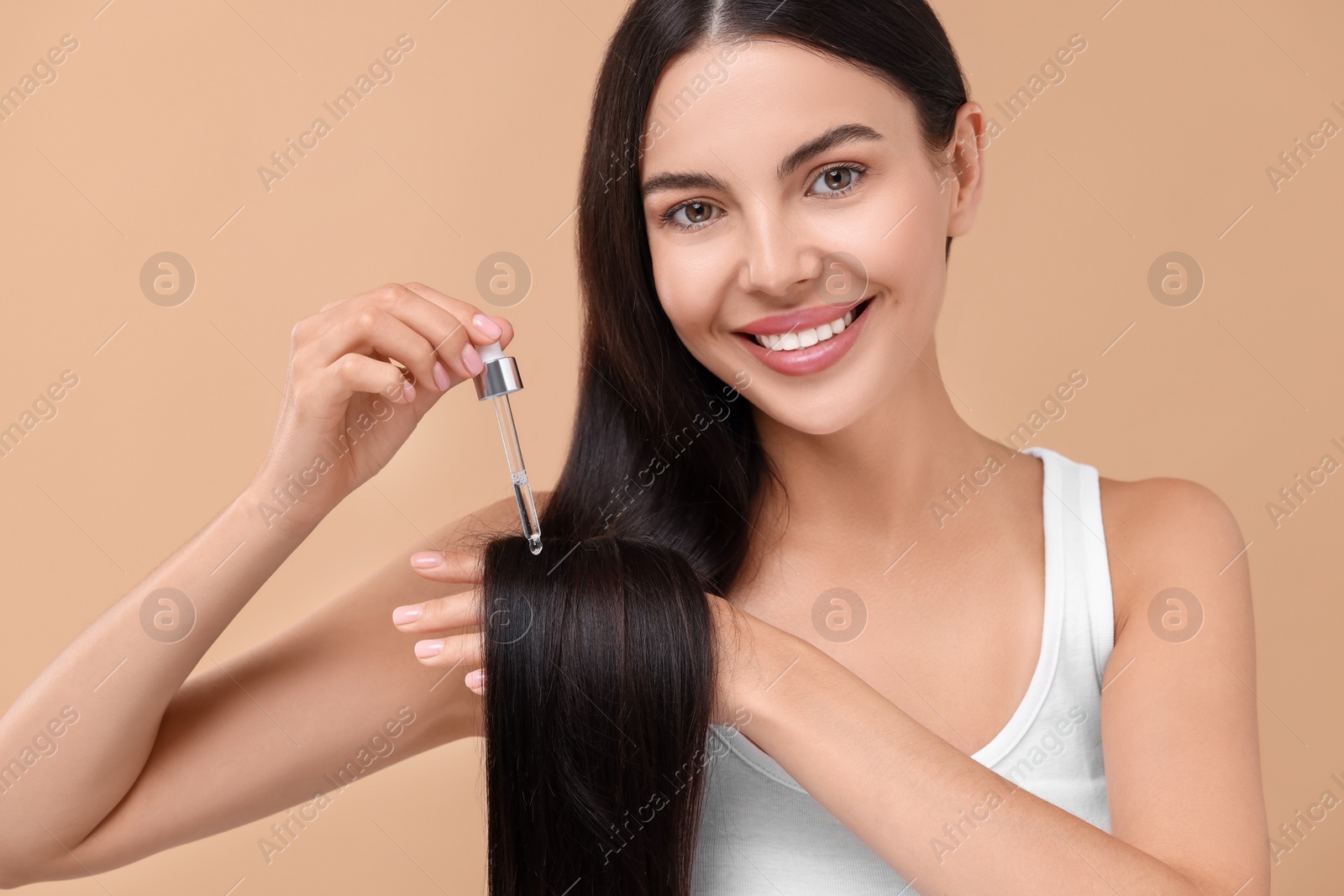 Photo of Beautiful woman applying hair serum on beige background. Cosmetic product