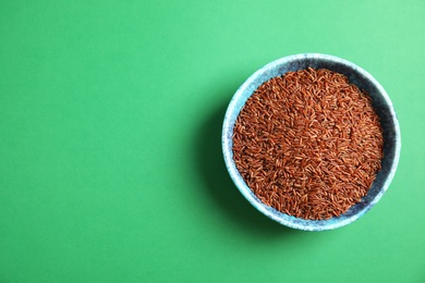 Bowl with uncooked red rice on color background, top view. Space for text