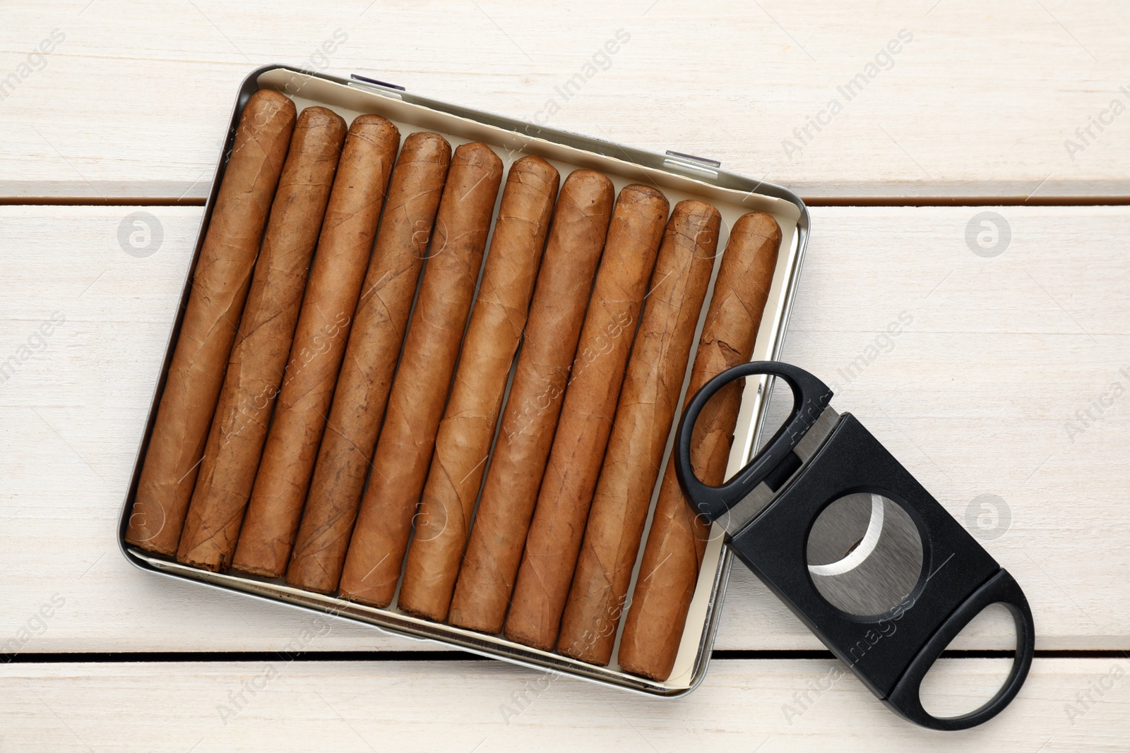 Photo of Cigars and guillotine cutter on white wooden table, flat lay