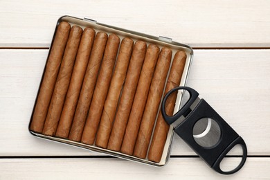 Photo of Cigars and guillotine cutter on white wooden table, flat lay