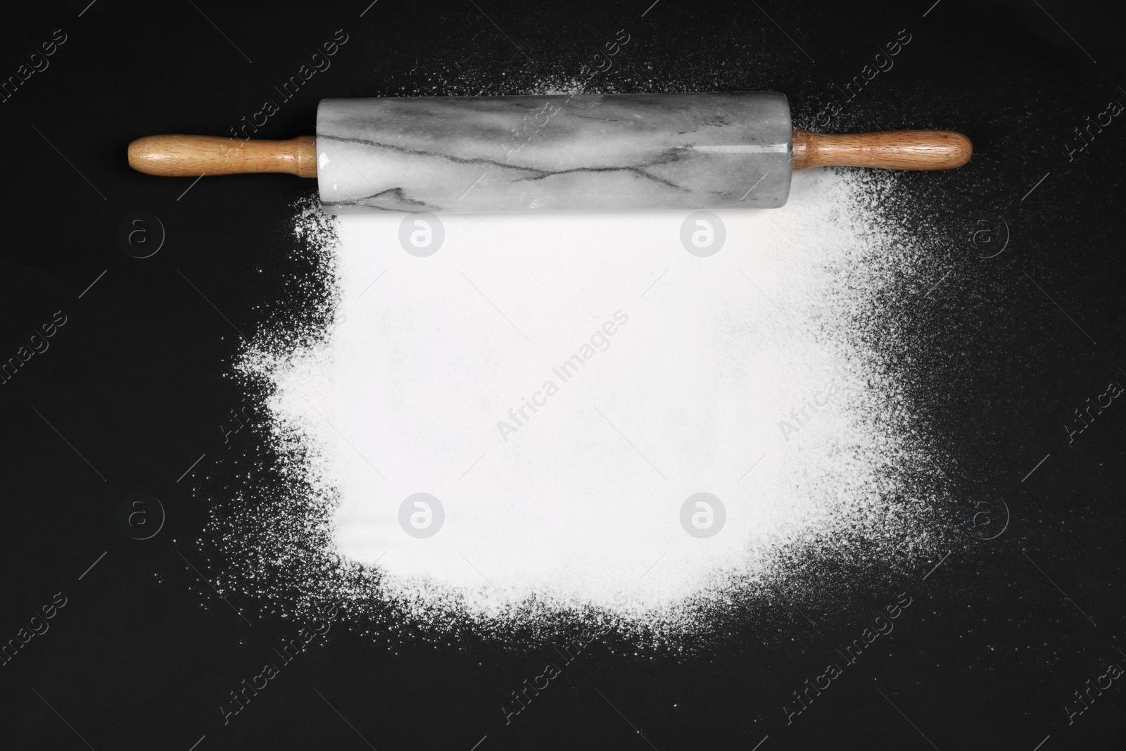 Photo of Flour and rolling pin on black table, flat lay