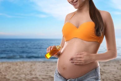 Young pregnant woman with sun protection cream on beach, closeup. Space for text