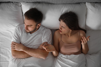 Photo of Young couple quarreling in bed at home, top view. Relationship problems