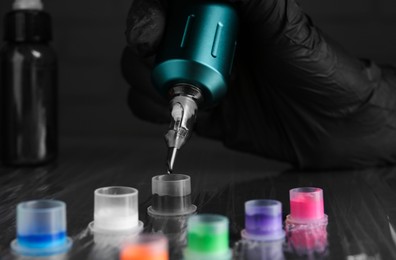 Photo of Tattoo artist with professional machine and colorful inks at table, closeup