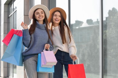 Beautiful young women with shopping bags near building outdoors