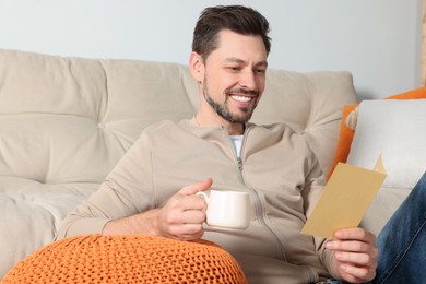 Photo of Happy man reading greeting card while drinking coffee in living room