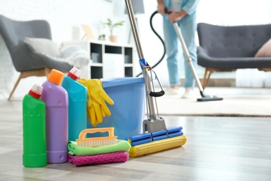 Photo of Detergents, bucket and mop on floor with janitor vacuuming carpet indoors