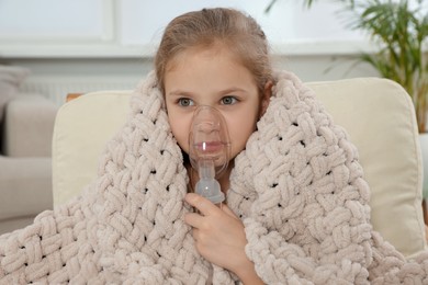 Photo of Little girl using nebulizer for inhalation in armchair at home