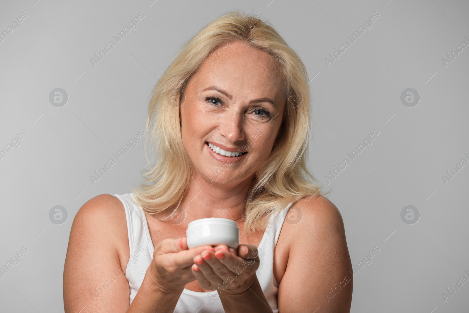 Photo of Portrait of beautiful mature woman with perfect skin holding jar of cream on grey background
