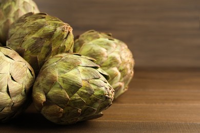 Photo of Fresh raw artichokes on wooden table, closeup. Space for text