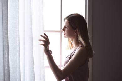 Lonely depressed woman near window at home