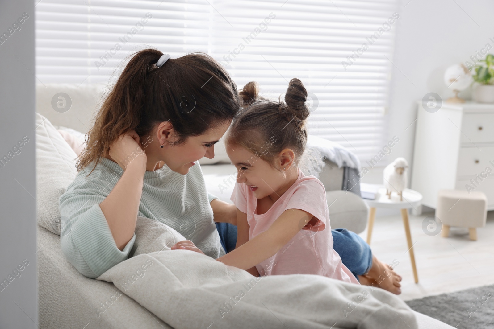 Photo of Young mother and her daughter spending time together on sofa at home