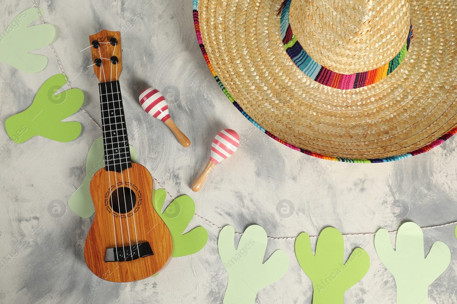 Photo of Mexican sombrero hat, ukulele and maracas on grey textured table, flat lay