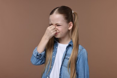 Little girl suffering from headache on brown background
