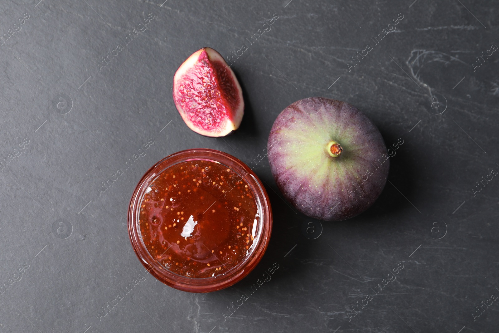 Photo of Jar of tasty fig jam and fresh fruits on black table, flat lay