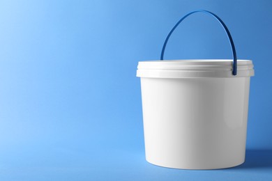 Photo of One plastic bucket with lid on light blue background. Space for text