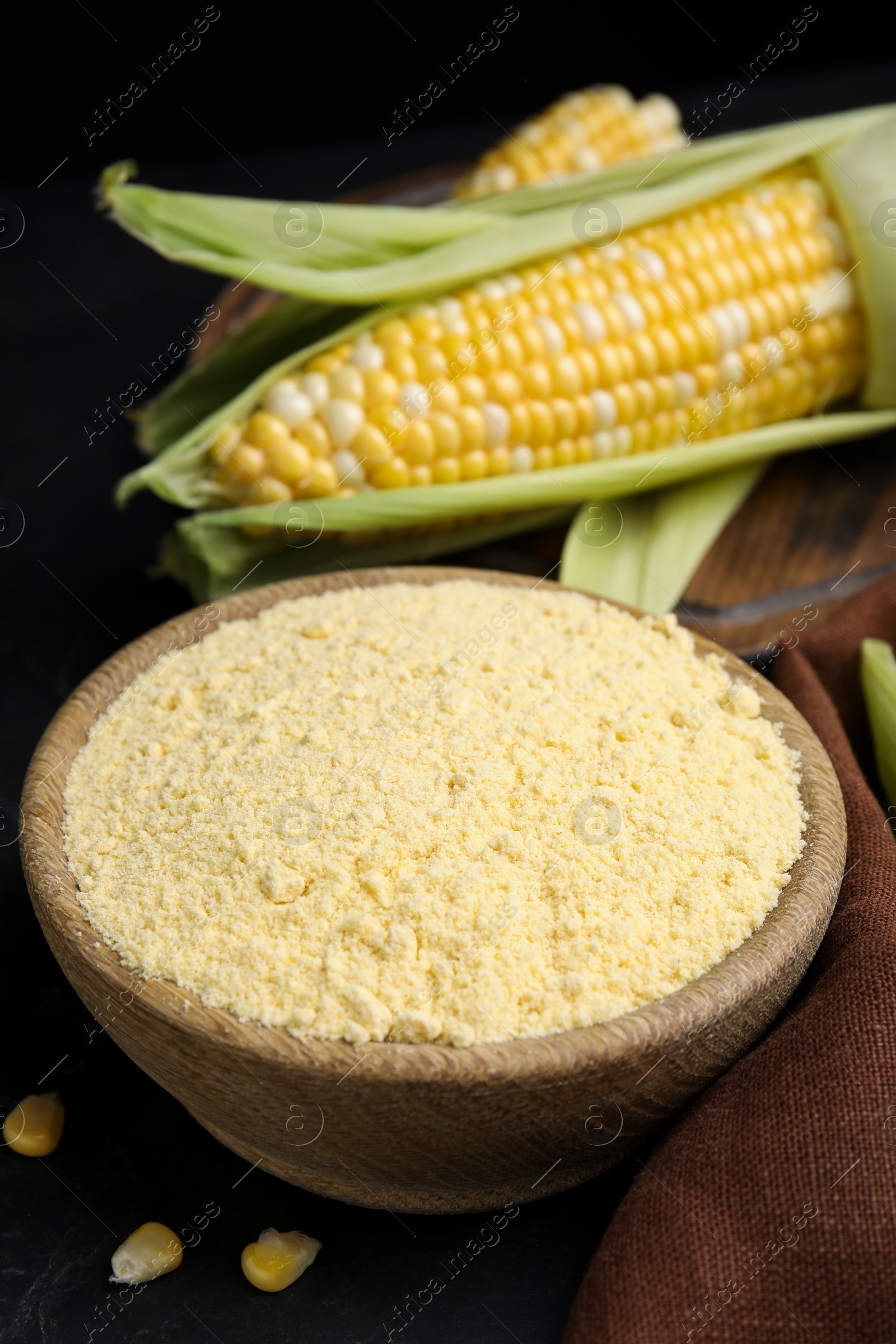 Photo of Corn flour in bowl and fresh cobs on black table