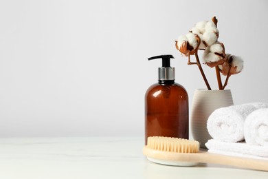 Different bath accessories and cotton flowers in vase on light table against white wall, space for text