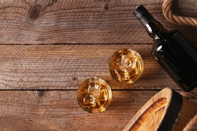Photo of Whiskey with ice cubes in glasses, bottle and barrel on wooden table, flat lay. Space for text
