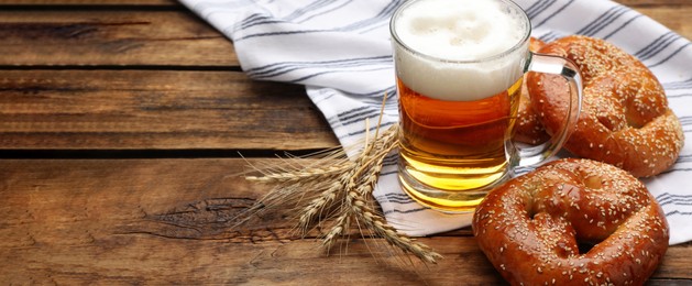 Image of Tasty pretzels, glass of beer and wheat spikes on wooden table, space for text. Banner design