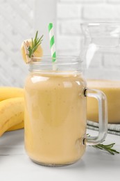 Mason jar of tasty banana smoothie with straw on white marble table