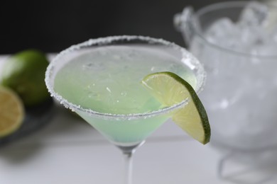 Delicious Margarita cocktail with ice cubes in glass and lime on table, closeup