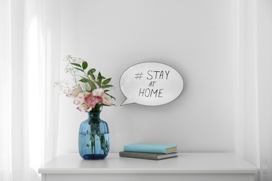 Flowers, books and speech bubble with hashtag STAY AT HOME indoors. Message to promote self-isolation during COVID‑19 pandemic