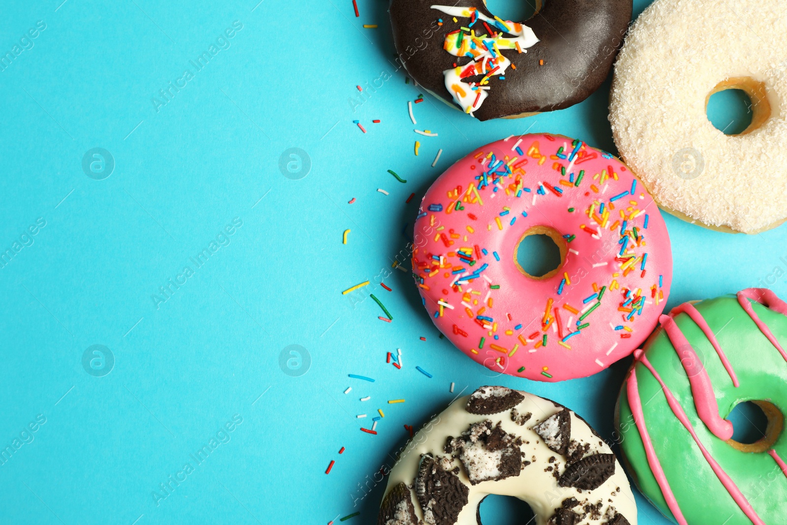 Photo of Different delicious glazed doughnuts on light blue background, flat lay. Space for text