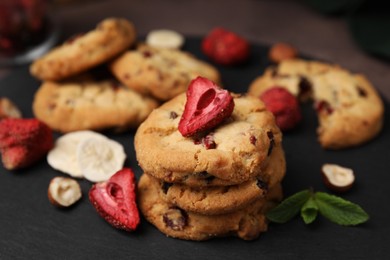 Photo of Cookies with freeze dried fruits, mint and nuts on black board, closeup