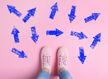 Choosing future profession. Girl standing in front of drawn signs on pink background, top view. Arrows pointing in different directions symbolizing diversity of opportunities