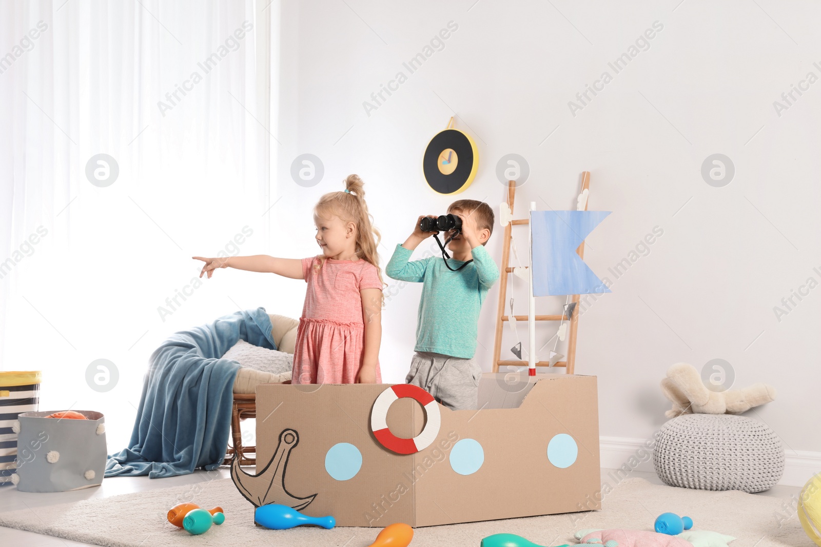 Photo of Cute little children playing with cardboard ship at home