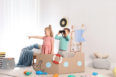 Cute little children playing with cardboard ship at home
