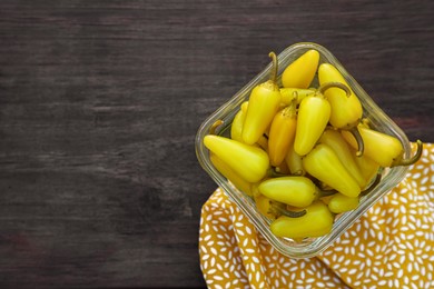 Photo of Bowl of pickled yellow jalapeno peppers on wooden table, top view. Space for text