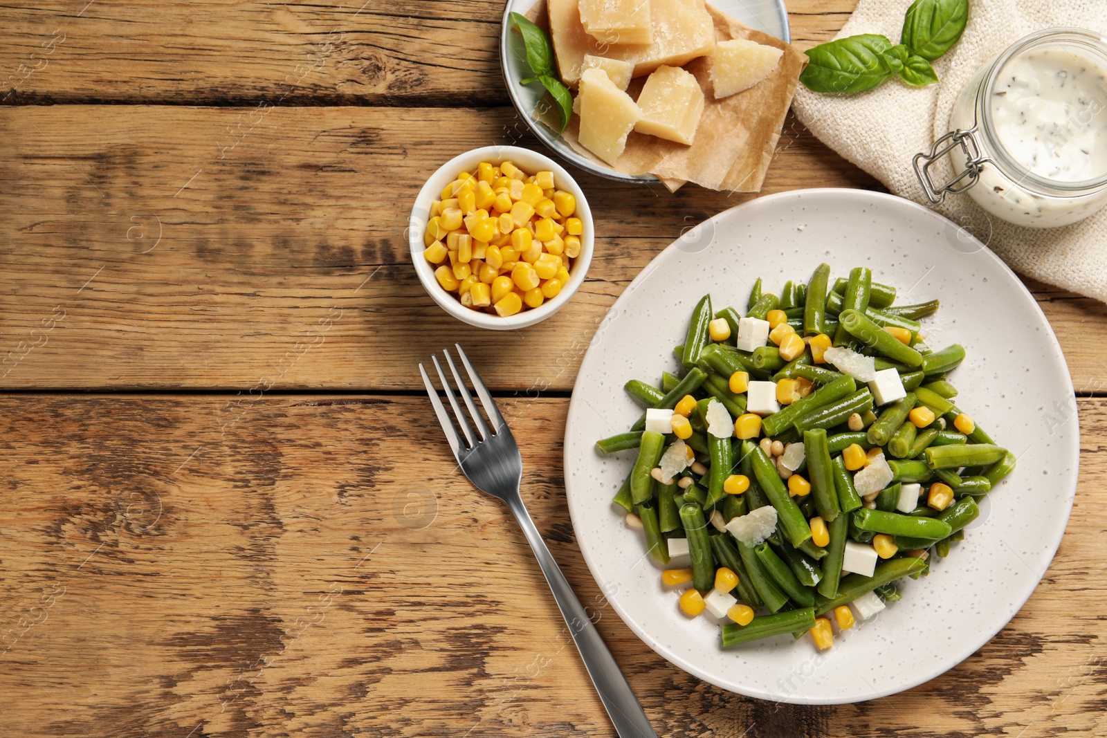 Photo of Delicious salad with green beans, corn and cheese served on wooden table, flat lay. Space for text
