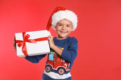 Happy little child in Santa hat with gift box on red background. Christmas celebration