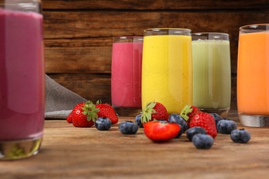 Glasses with different tasty smoothies and ingredients on wooden table