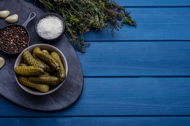 Photo of Bowl of pickled cucumbers and ingredients on blue wooden table, flat lay. Space for text