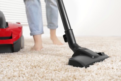 Woman cleaning carpet with vacuum cleaner at home, closeup