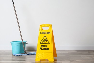 Photo of Safety sign with phrase Caution wet floor, mop and bucket indoors. Cleaning service