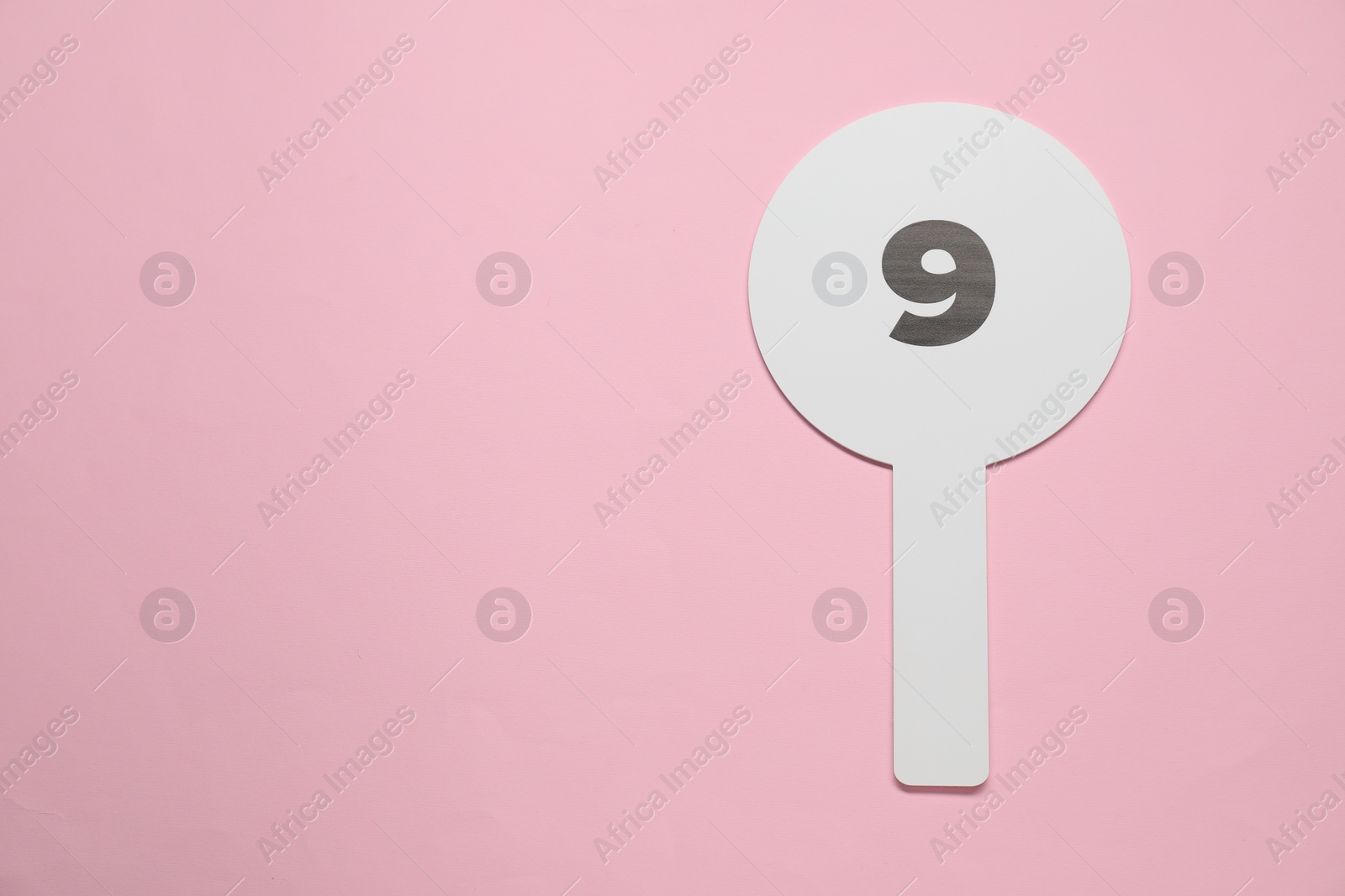 Photo of Auction paddle with number 9 on pink background, top view. Space for text