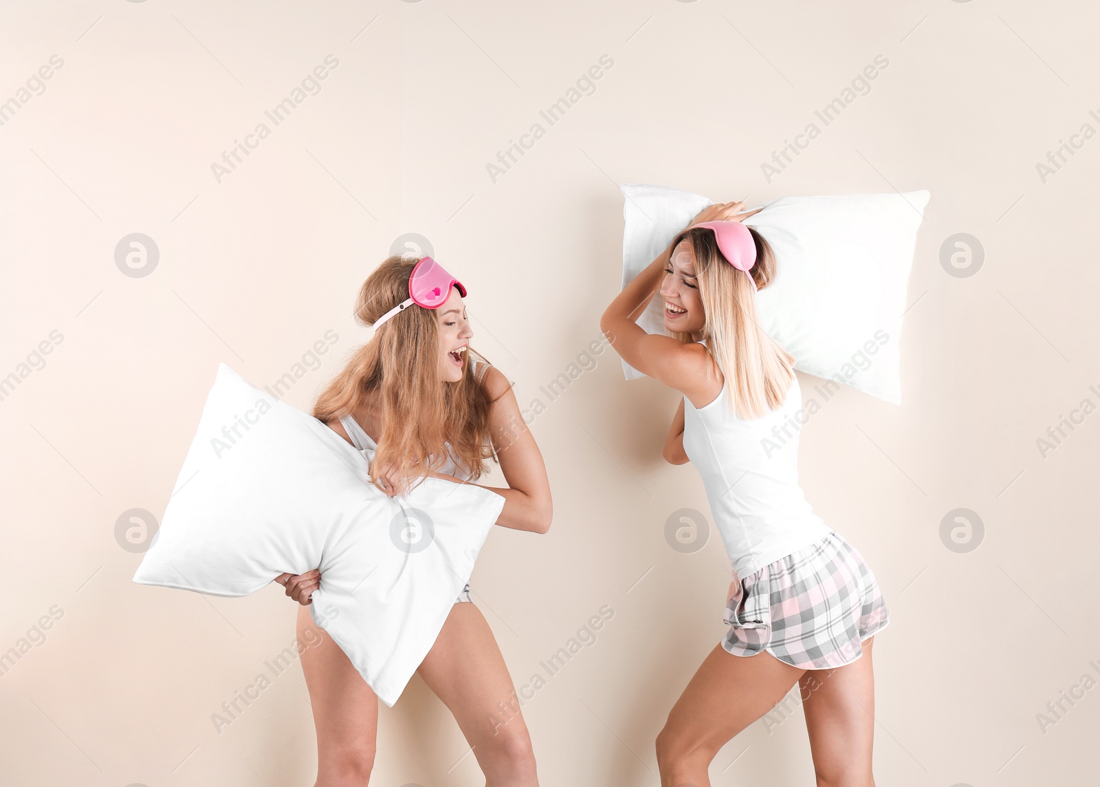 Photo of Two young women having pillow fight against color background