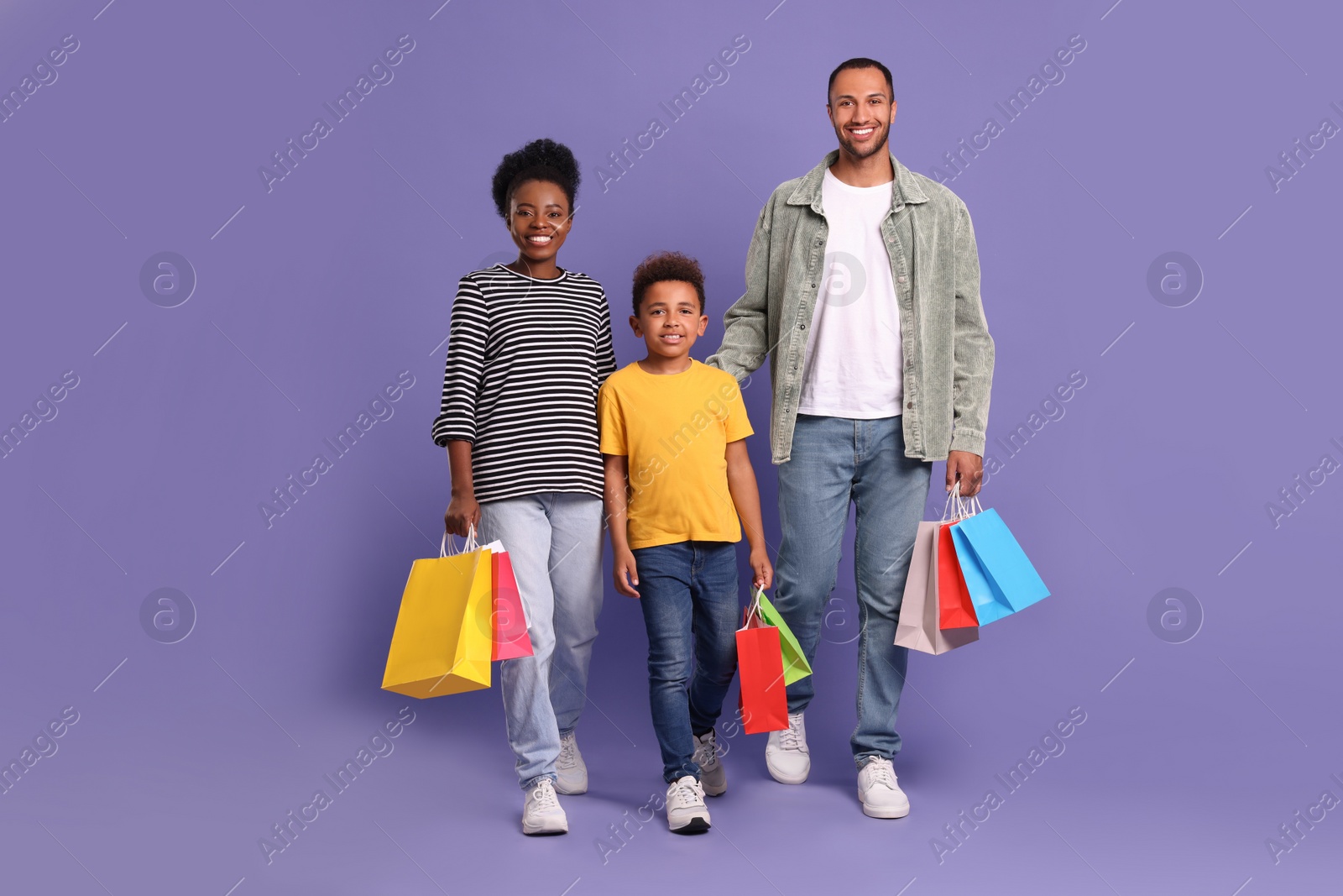 Photo of Family shopping. Happy parents and son with colorful bags on violet background