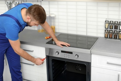 Professional serviceman repairing modern oven in kitchen