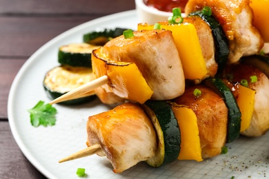 Photo of Delicious chicken shish kebabs with vegetables on wooden table, closeup