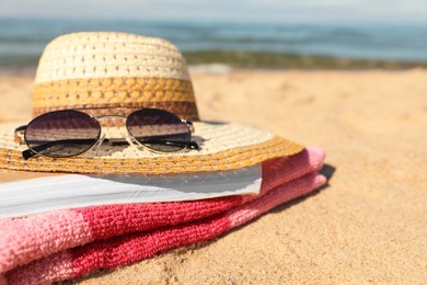 Hat, sunglasses, book and striped towel on sandy beach near sea, closeup. Space for text